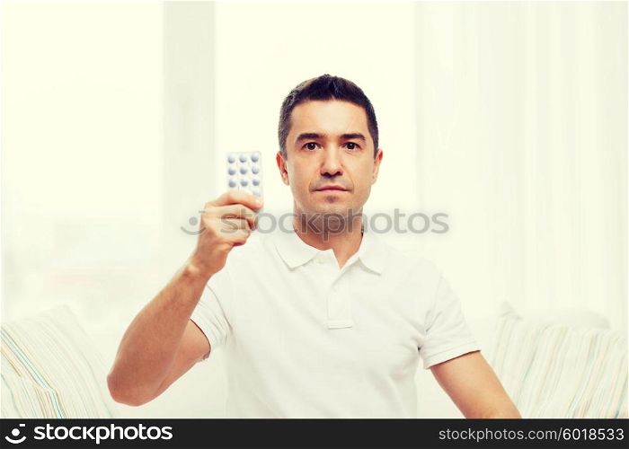 people, medication, medicine and health care concept - man showing pack of pills at home