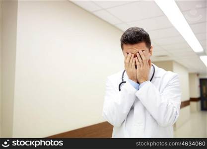 people, medicine, healthcare and sorrow concept - sad or crying male doctor at hospital corridor