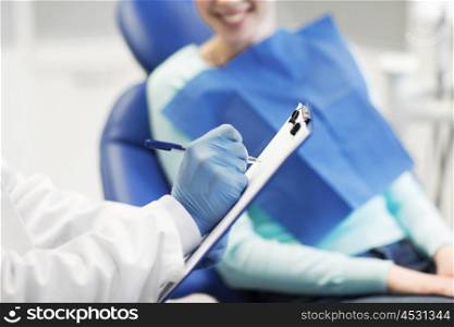 people, medicine, stomatology and health care concept - close up of dentist with clipboard and happy patient woman at dental clinic office