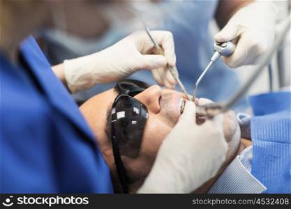 people, medicine, stomatology and health care concept - close up of dentist and assistant hands with dental instrumnes treating male patient teeth at dental clinic office