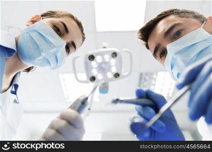people, medicine, stomatology and health care concept - close up of dentist and assistant with dental mirror, drill and air water gun spray treating patient teeth at dental clinic