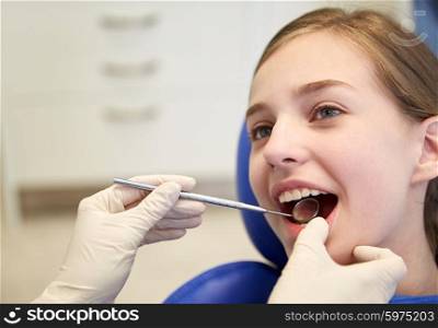 people, medicine, stomatology and health care concept - close up of dentist hands with dental mirror checking up patient girl teeth at clinic