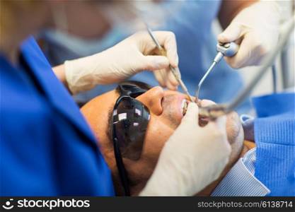 people, medicine, stomatology and health care concept - close up of dentist and assistant hands with dental instrumnes treating male patient teeth at dental clinic office
