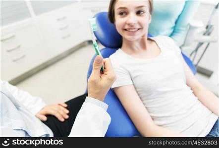 people, medicine, stomatology and health care concept -close up of dentist hand holding toothbrush and patient girl at dental clinic office