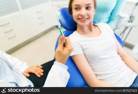 people, medicine, stomatology and health care concept -close up of dentist hand holding toothbrush and patient girl at dental clinic office