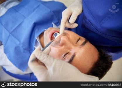 people, medicine, stomatology and health care concept - close up of female dentist with dental mirror checking up male patient teeth at dental clinic office