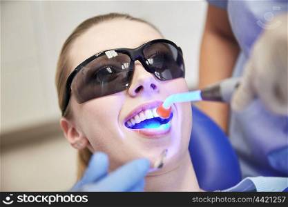 people, medicine, stomatology and health care concept - close up of woman patient in protective eyeglasses or goggles with dental curing light treating teeth at dental clinic office