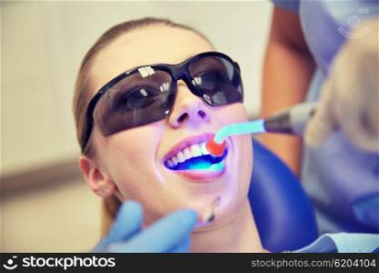 people, medicine, stomatology and health care concept - close up of woman patient in protective eyeglasses or goggles with dental curing light treating teeth at dental clinic office
