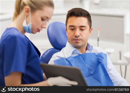 people, medicine, stomatology and health care concept - female dentist showing tablet pc computer to male patient at dental clinic office