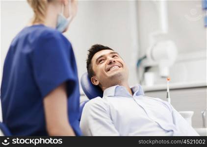 people, medicine, stomatology and health care concept - female dentist talking to happy male patient at dental clinic office