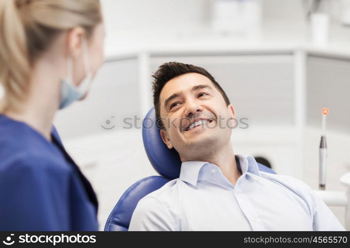 people, medicine, stomatology and health care concept - female dentist talking to happy male patient at dental clinic office