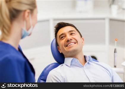 people, medicine, stomatology and health care concept - female dentist talking to happy male patient at dental clinic office