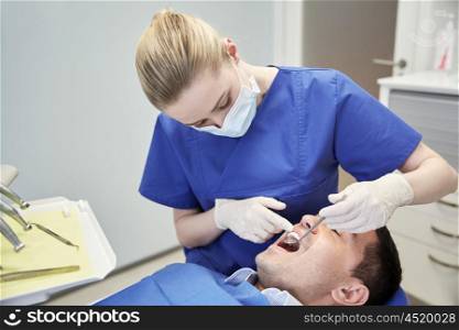 people, medicine, stomatology and health care concept - female dentist with dental mirror checking up male patient teeth at dental clinic office