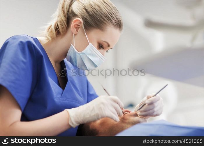 people, medicine, stomatology and health care concept - female dentist with dental mirror and probe checking up male patient teeth at dental clinic office