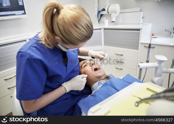 people, medicine, stomatology and health care concept - female dentist with dental mirror checking up male patient teeth at dental clinic office