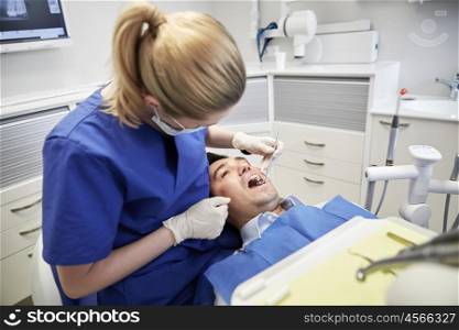 people, medicine, stomatology and health care concept - female dentist with dental mirror checking up male patient teeth at dental clinic office