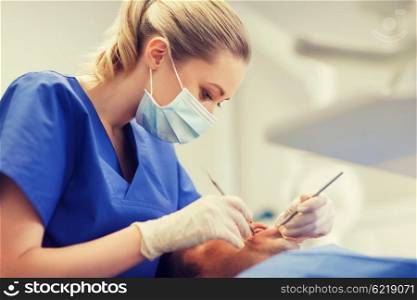 people, medicine, stomatology and health care concept - female dentist with dental mirror and probe checking up male patient teeth at dental clinic office