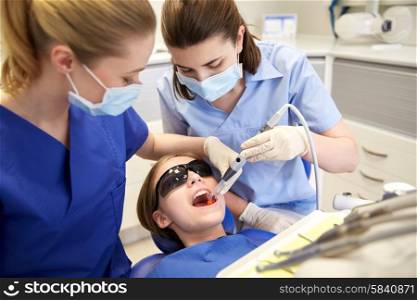 people, medicine, stomatology and health care concept - female dentists with mirror and suction treating patient girl teeth at dental clinic office