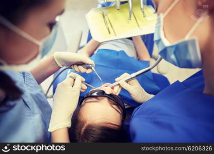 people, medicine, stomatology and health care concept - female dentists with mirror, drill and probe treating patient girl teeth at dental clinic office