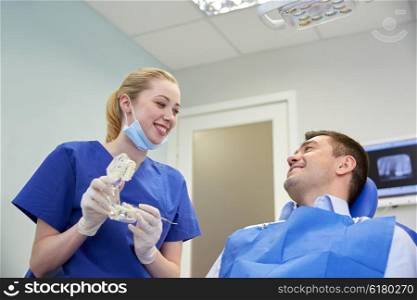 people, medicine, stomatology and health care concept - happy fe male dentist showing jaw layout to male patient at dental clinic office