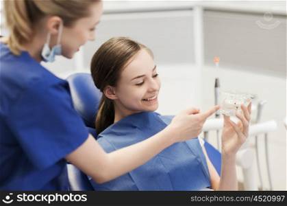 people, medicine, stomatology and health care concept - happy female dentist showing jaw layout to patient girl at dental clinic office