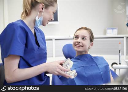 people, medicine, stomatology and health care concept - happy female dentist showing jaw model to patient girl at dental clinic office