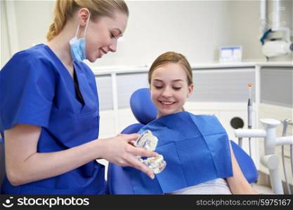people, medicine, stomatology and health care concept - happy female dentist showing jaw model to patient girl at dental clinic office