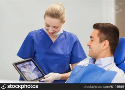 people, medicine, stomatology and health care concept - happy female dentist showing x-ray on tablet pc computer to male patient at dental clinic office