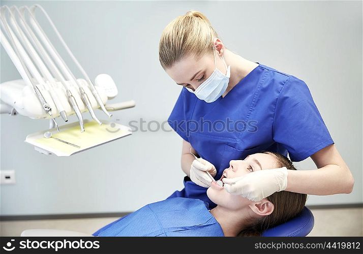 people, medicine, stomatology and health care concept - happy female dentist with mirror and probe checking patient girl teeth up at dental clinic office
