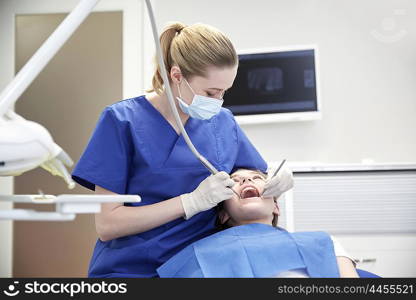 people, medicine, stomatology and health care concept - happy female dentist with dental tools checking patient girl teeth up at dental clinic office