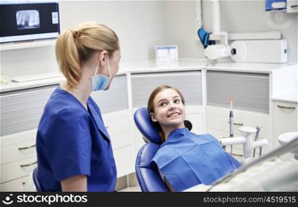 people, medicine, stomatology and health care concept - happy female dentist with patient girl talking at dental clinic office