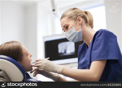 people, medicine, stomatology and health care concept - happy female dentist with mirror or dental probe checking patient girl teeth up at dental clinic office