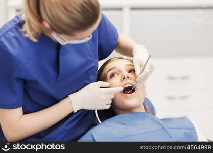 people, medicine, stomatology and health care concept - happy female dentist with mirror checking patient girl teeth up at dental clinic office