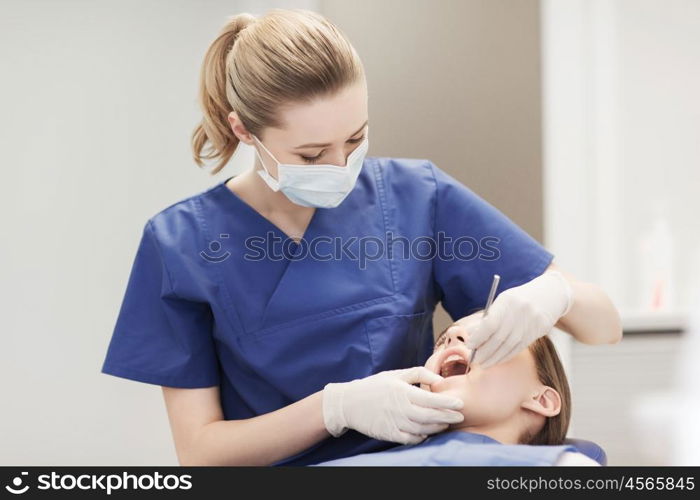 people, medicine, stomatology and health care concept - happy female dentist with mirror checking patient girl teeth up at dental clinic office