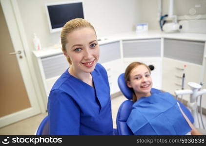 people, medicine, stomatology and health care concept - happy female dentist with patient girl at dental clinic office