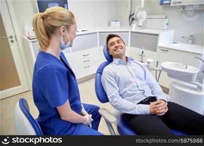 people, medicine, stomatology and health care concept - happy female dentist with man patient talking at dental clinic office