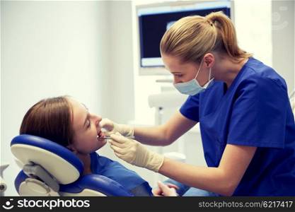 people, medicine, stomatology and health care concept - happy female dentist with mirror checking patient girl teeth up at dental clinic office