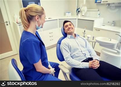 people, medicine, stomatology and health care concept - happy female dentist with man patient talking at dental clinic office