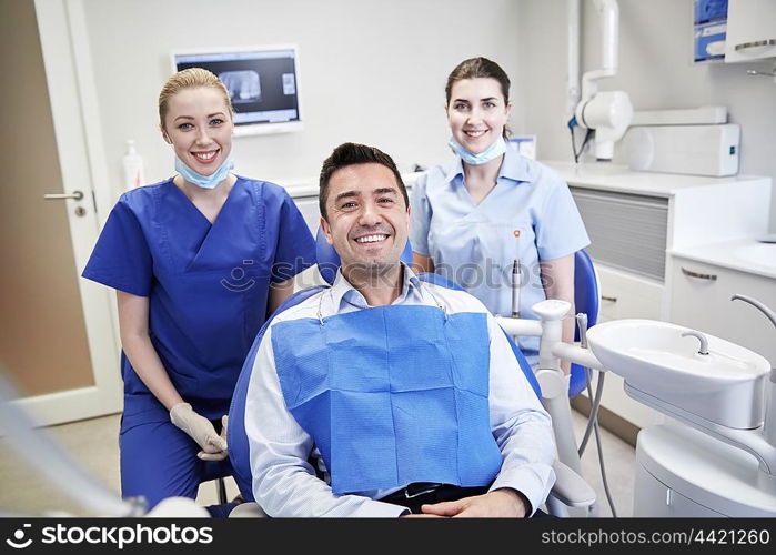 people, medicine, stomatology and health care concept - happy female dentists with man patient at dental clinic office