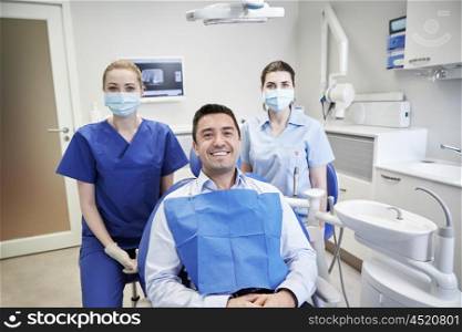 people, medicine, stomatology and health care concept - happy female dentists with man patient at dental clinic office