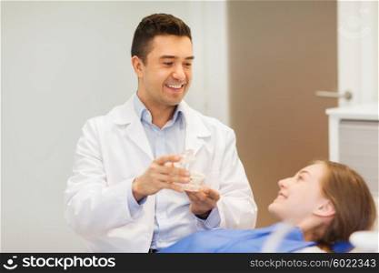 people, medicine, stomatology and health care concept - happy male dentist showing jaw layout to patient girl at dental clinic office