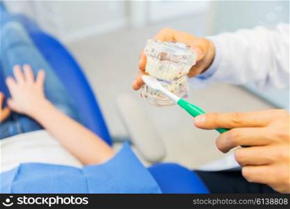 people, medicine, stomatology and health care concept - happy male dentist showing jaw and teeth layout to patient girl at dental clinic office