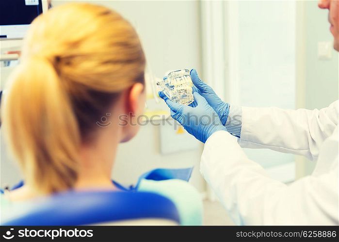 people, medicine, stomatology and health care concept - happy male dentist showing jaw and teeth layout to patient woman at dental clinic office