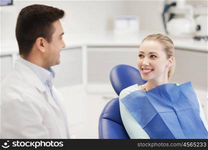 people, medicine, stomatology and health care concept - happy male dentist with woman patient talking at dental clinic office
