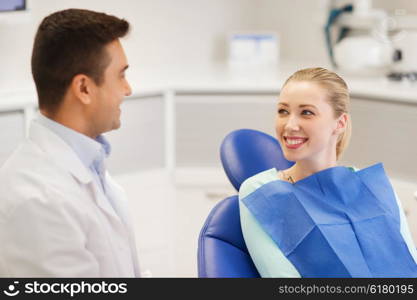 people, medicine, stomatology and health care concept - happy male dentist with woman patient talking at dental clinic office