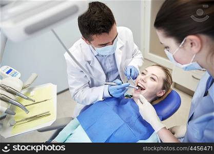 people, medicine, stomatology and health care concept - male dentist and assistant with dental mirror, drill and air water gun spray treating female patient teeth at dental clinic