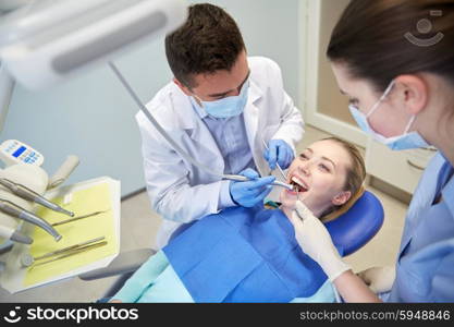 people, medicine, stomatology and health care concept - male dentist and assistant with dental mirror, drill and air water gun spray treating female patient teeth at dental clinic