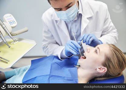 people, medicine, stomatology and health care concept - male dentist in mask with dental mirror and probe checking female patient teeth up at dental clinic office