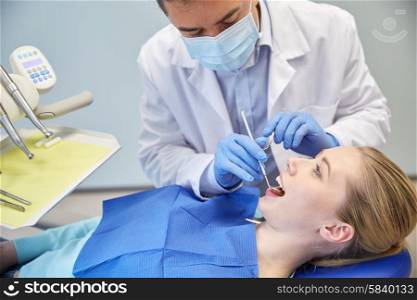 people, medicine, stomatology and health care concept - male dentist in mask with dental mirror and probe checking female patient teeth up at dental clinic office