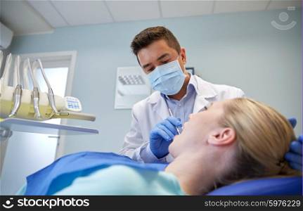 people, medicine, stomatology and health care concept - male dentist in mask checking female patient teeth up at dental clinic office
